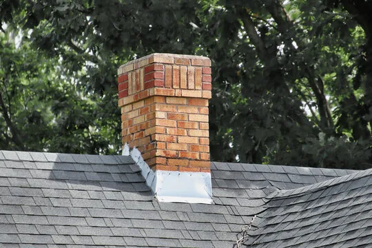 Brick chimney with contrasting decorative bands and a corbelled top, framed by trees